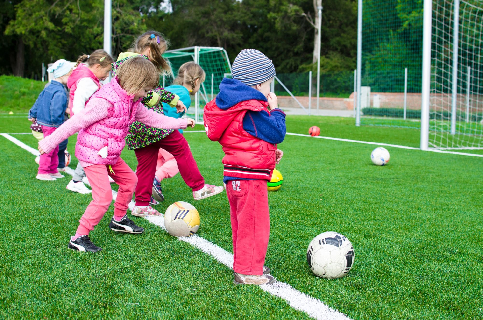 Bambini piccoli che giocano con il pallone su campo in sintetico